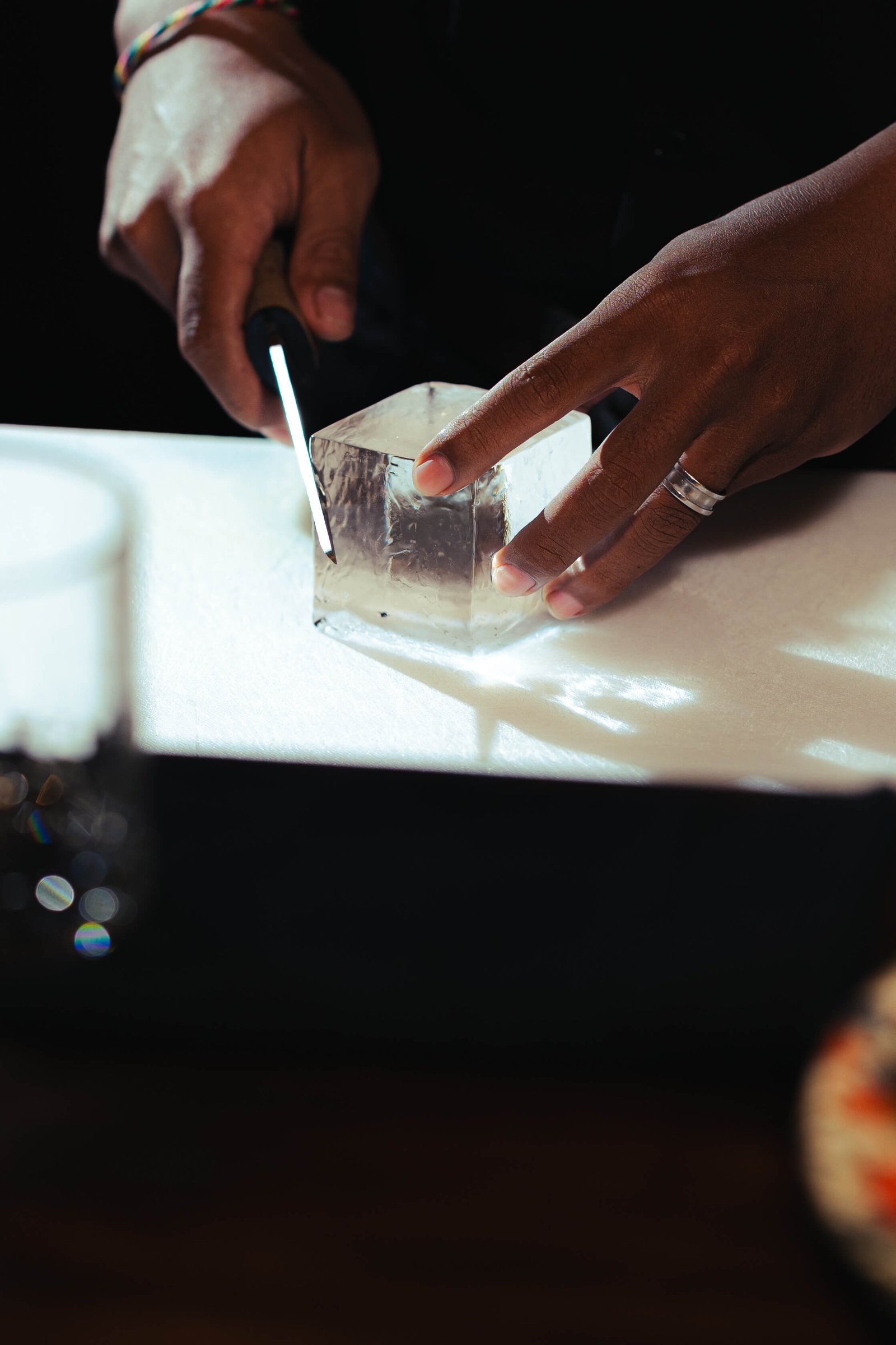 Hands hand-cutting a clear ice cube to precise dimensions